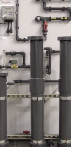 Industrial plumbing system with vertical pipes, valves, and control panel on a white wall.