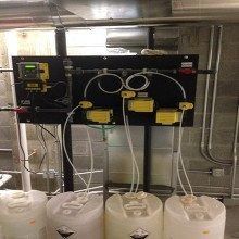 Chemical dosing system with tanks, pumps, and control panel. White tubing connects to yellow boxes.