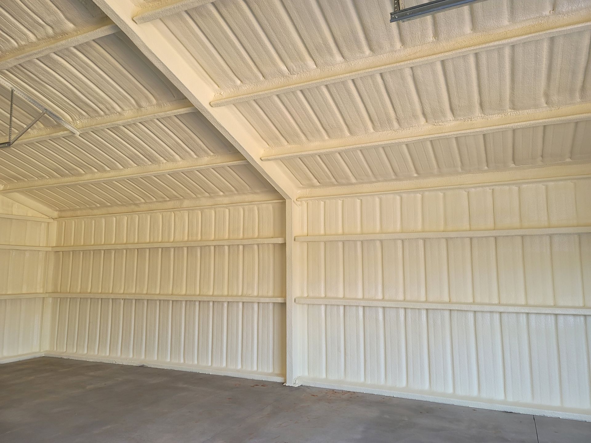 A large empty garage with a ceiling and walls covered in white spray foam.