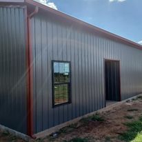 A gray metal building with a red gutter and a window.