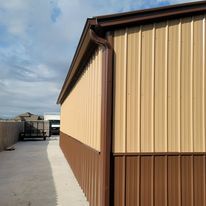 A brown and tan metal building with a gutter on the side.