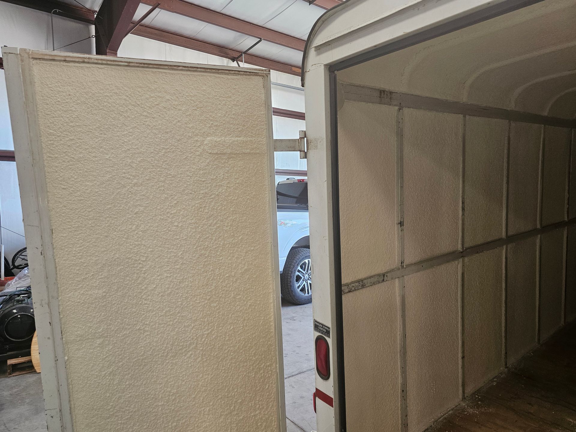 A trailer with the doors open and a truck parked in the background.