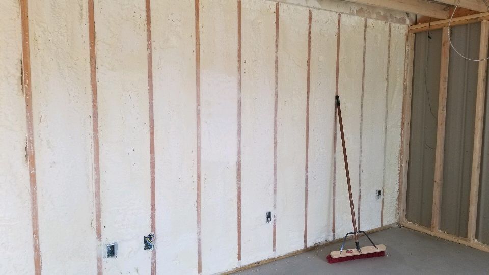 A room with a broom sitting in front of a wall covered in insulation.