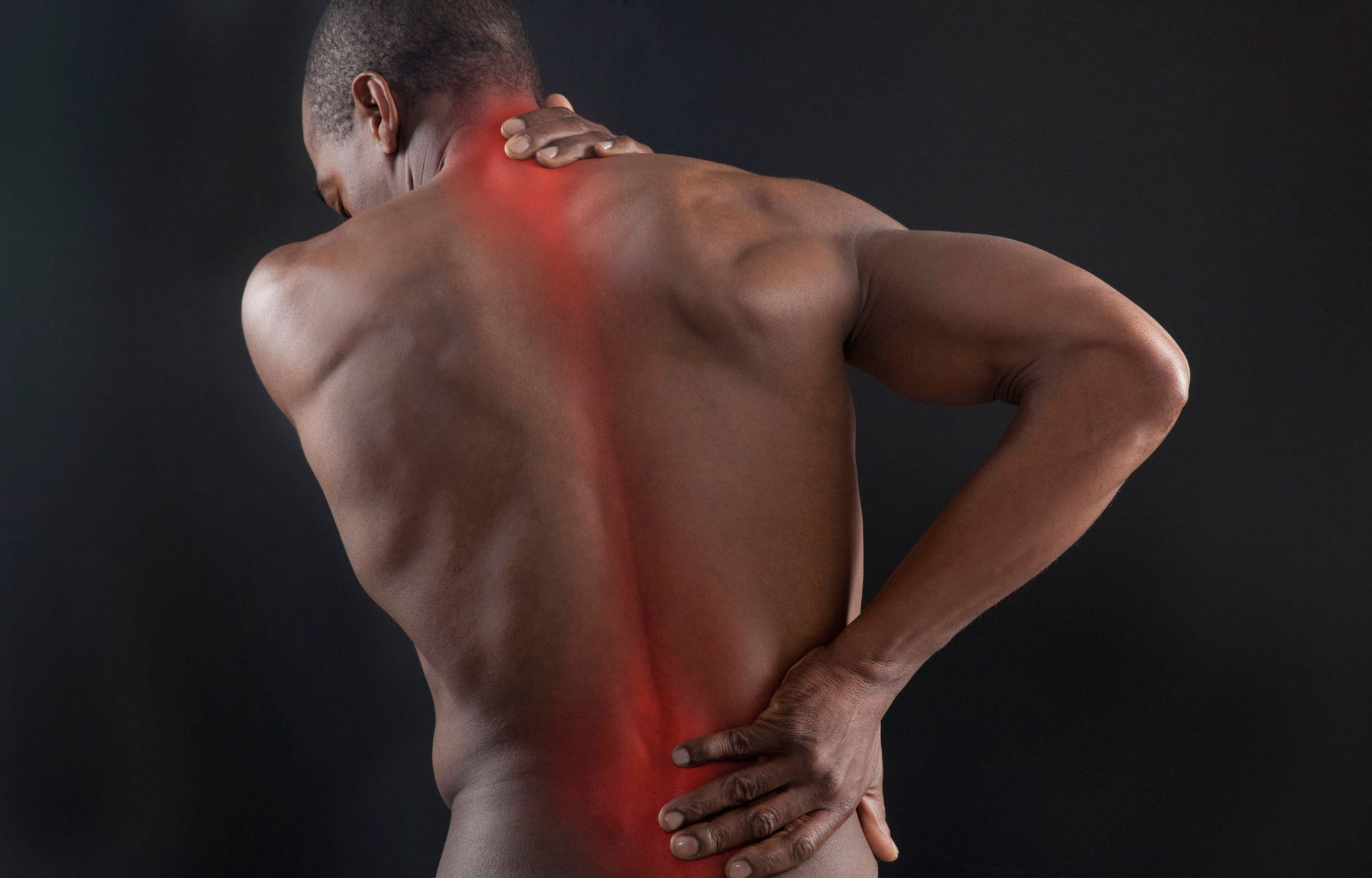 A shirtless man facing away and holding his neck and back with each hand.