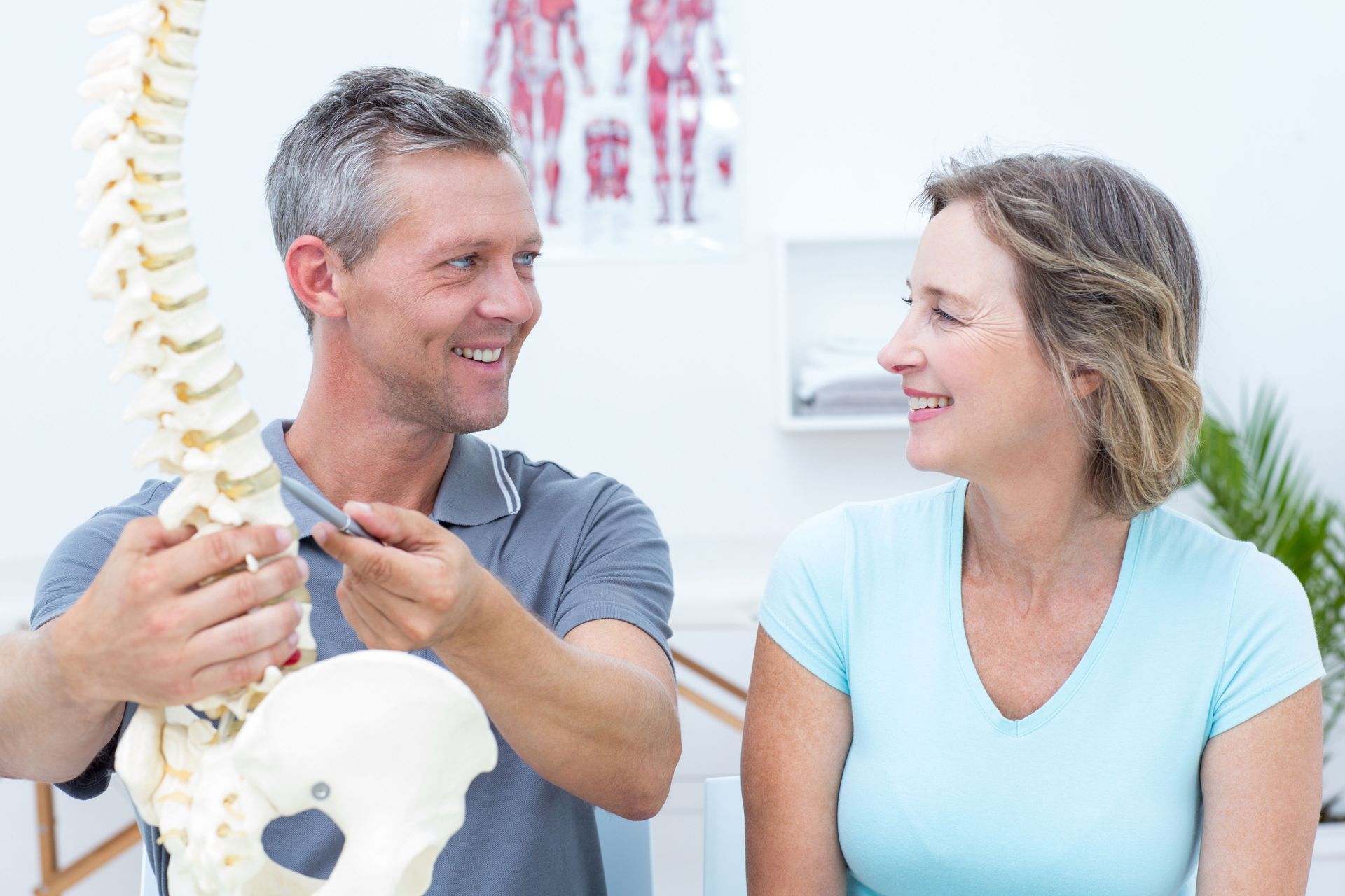 A man holding a spine and pointing to a vertebra while looking at a woman.