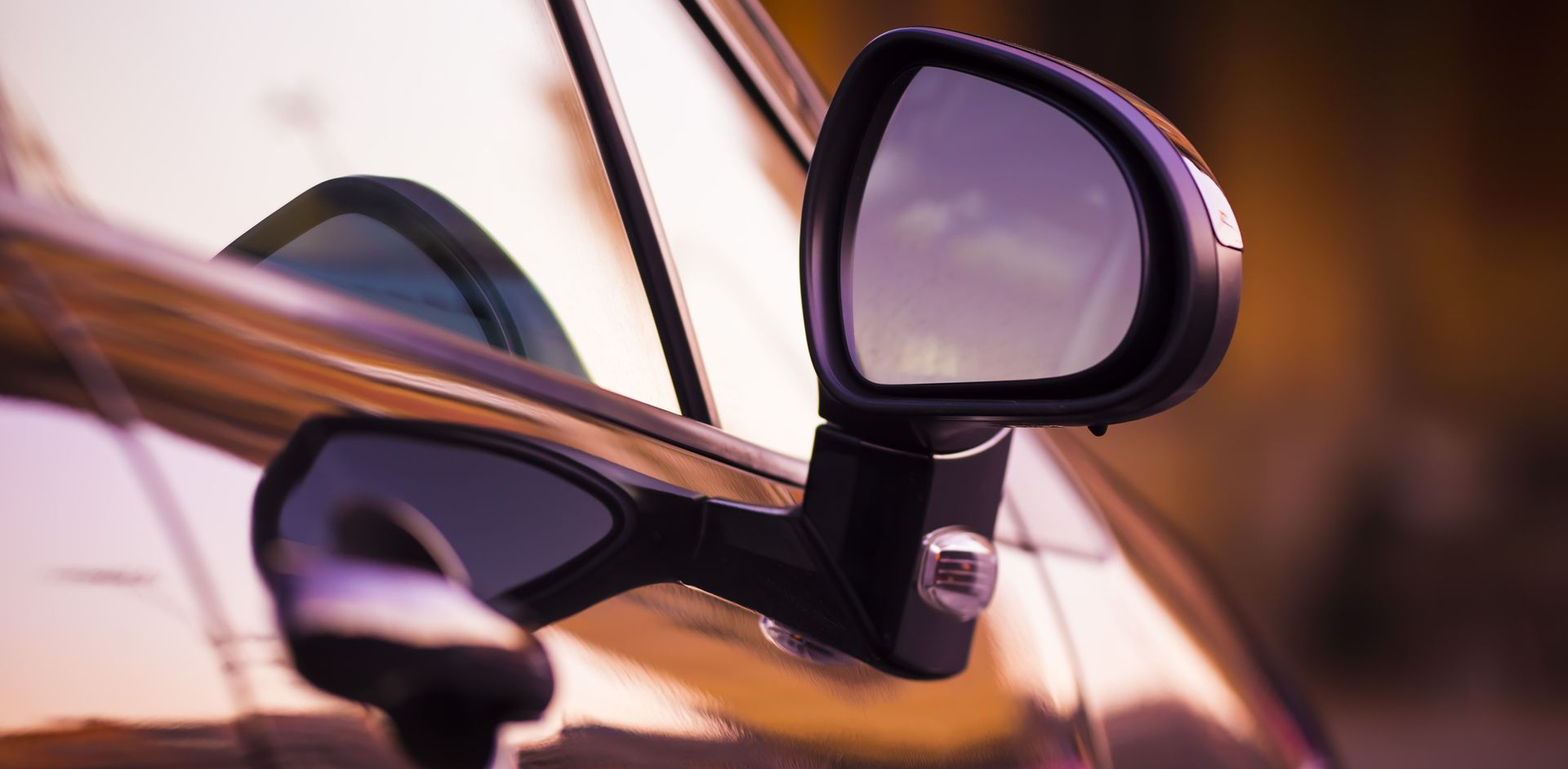 Close-up of a black car's side mirror, reflecting a colorful sunset.