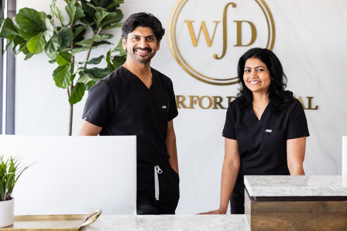 Two people in black scrubs stand behind a white counter 