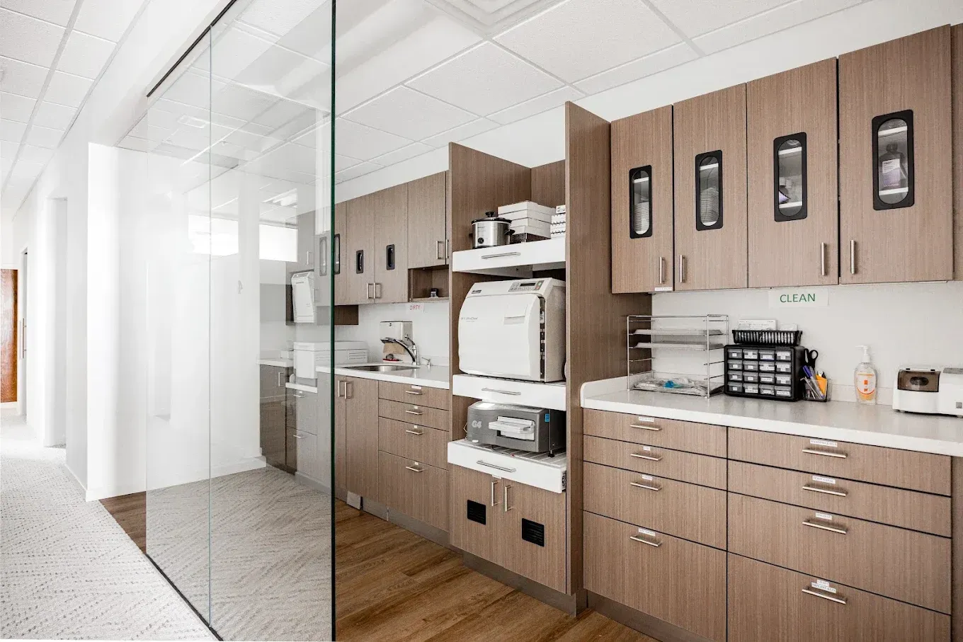 Dental office, cabinets, equipment, white countertops, glass wall, and hallway visible.
