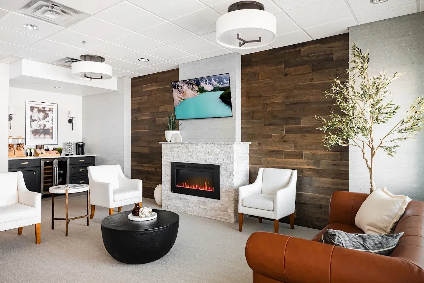 Cozy waiting room with white chairs, a fireplace, and a large brown leather couch.