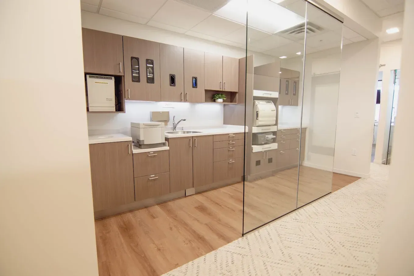 A dental office sterilization room with wooden cabinets, a sink, and glass walls.