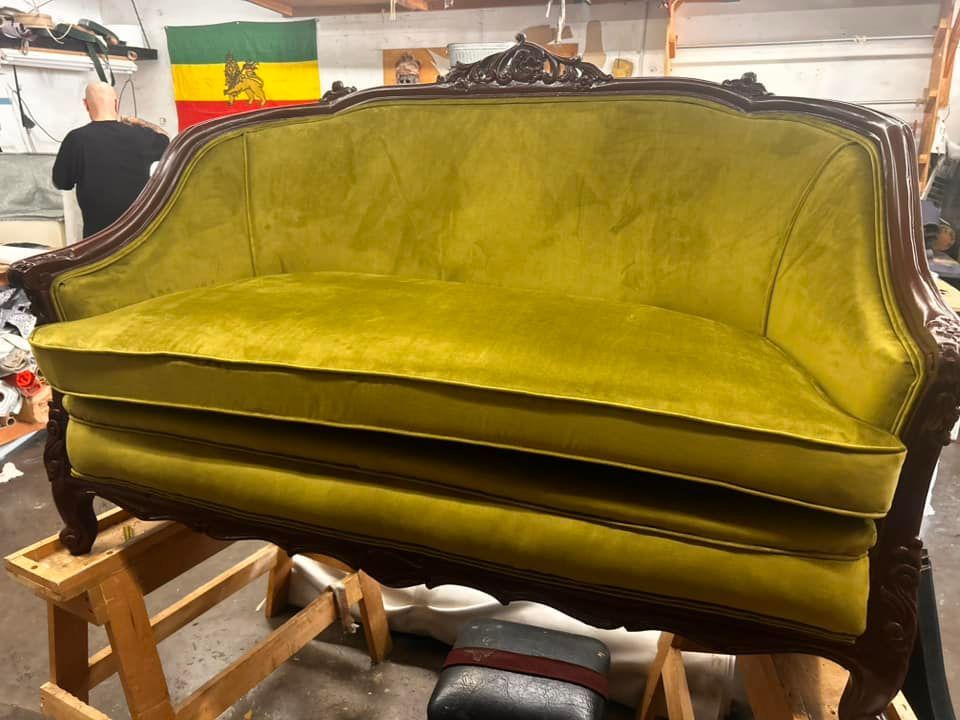 Green velvet antique sofa on wooden supports in a workshop.