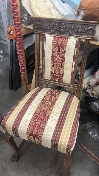 Upholstered wooden chair with ornate back. Seat and backrest have red and gold patterned fabric.