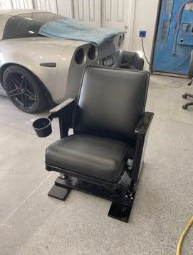 Black theater-style chair with a cupholder in a garage; a silver car is in the background.