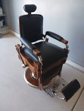 Vintage black and wood barber chair with headrest, armrests, and footrest.