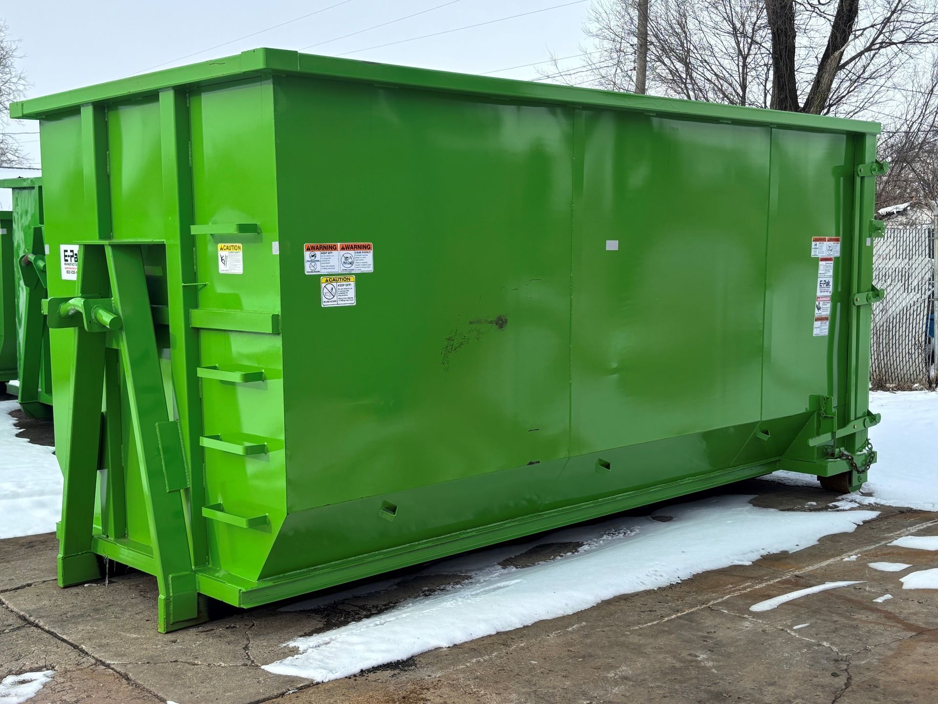 Green industrial dumpster on a snow-covered ground.