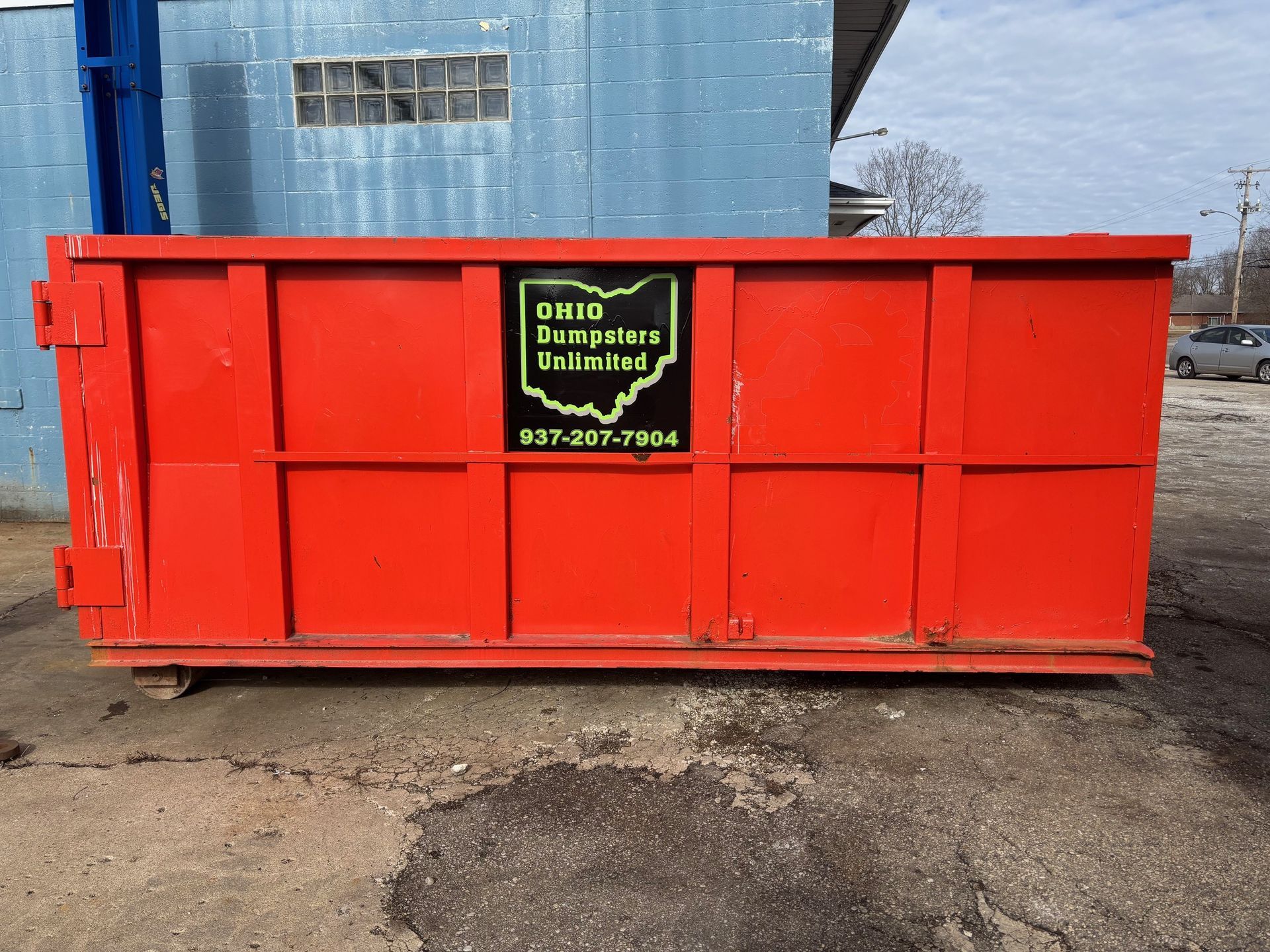 Red Ohio Dumpsters roll-off dumpster in front of a blue building with a logo that includes an outline of Ohio.