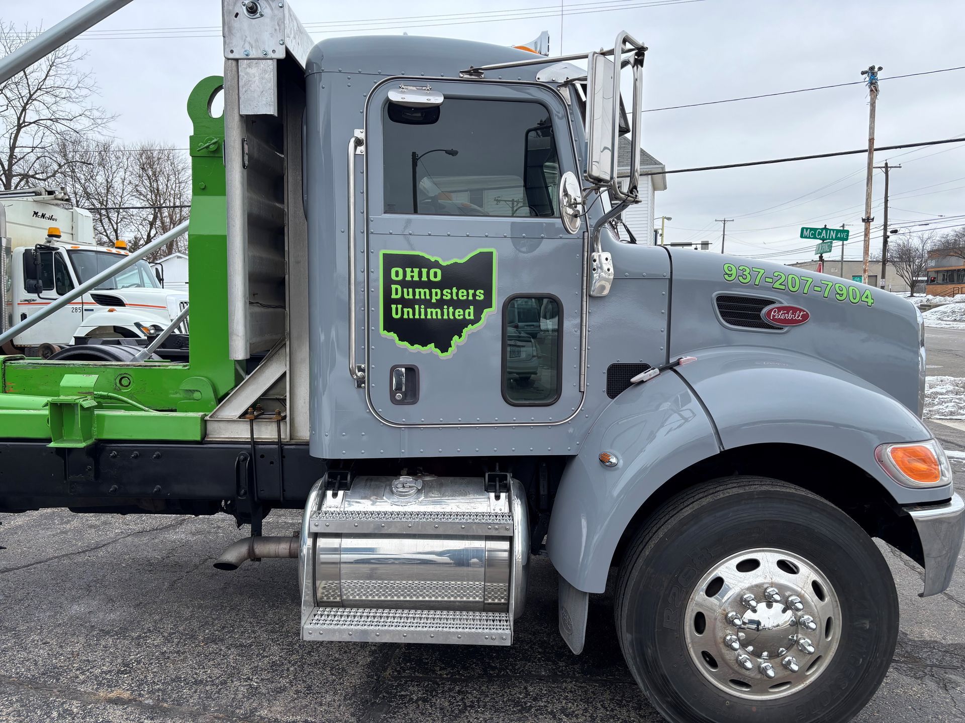 Gray Ohio Dumpsters Unlimited truck on a city street. Green dumpster bed is raised.