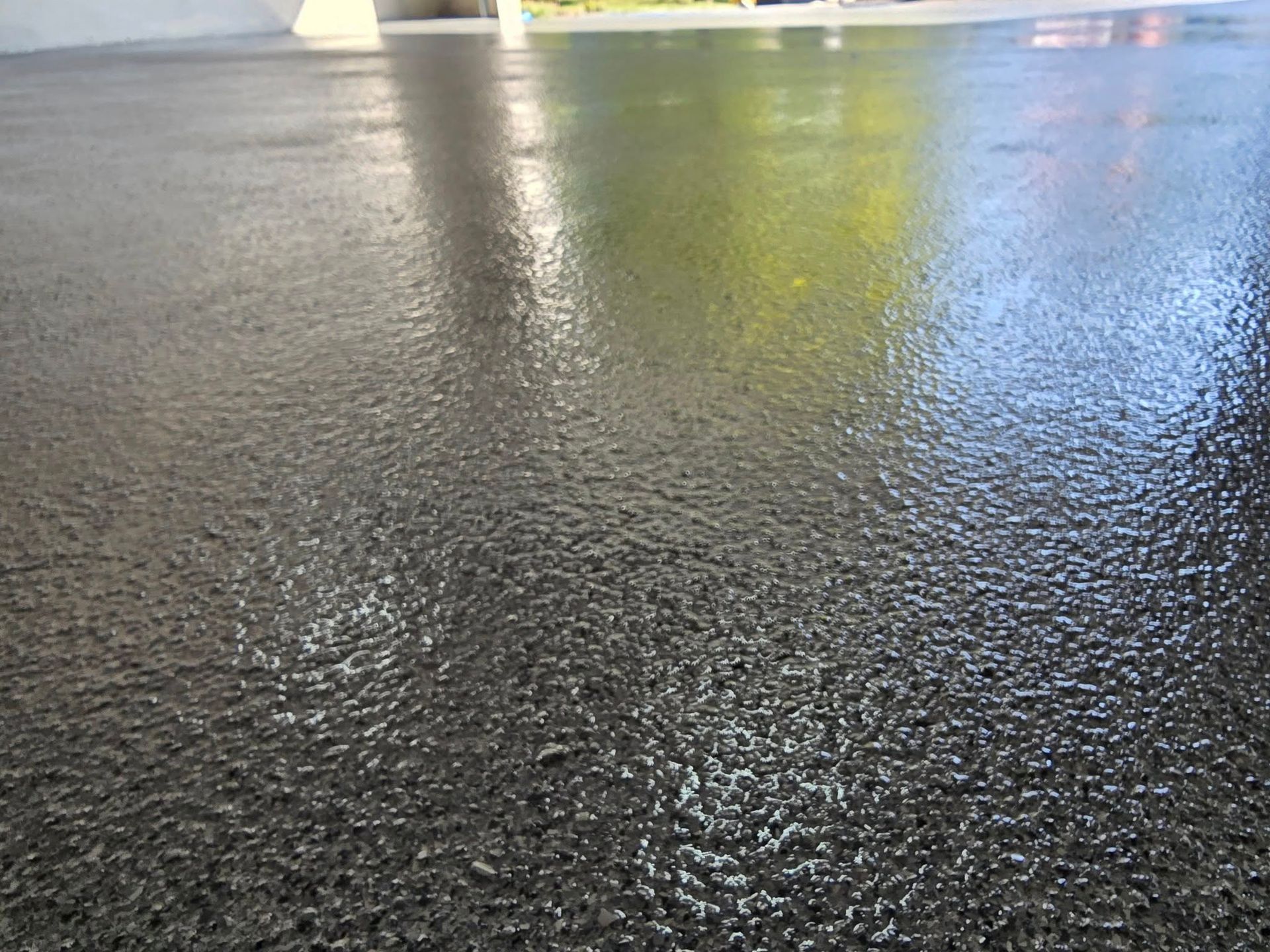 Close-up of a glossy, dark gray concrete floor reflecting sunlight and a blurred outdoor scene.