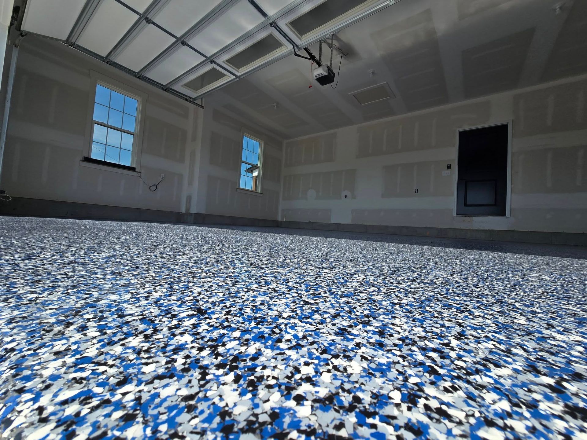 Garage with a blue, black, and white speckled floor, two windows, and a black door.