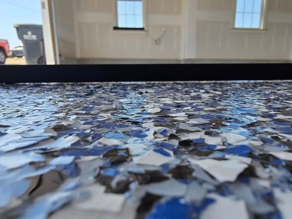 Close-up of a garage floor with blue, white, and black flakes. The garage interior is in the background.