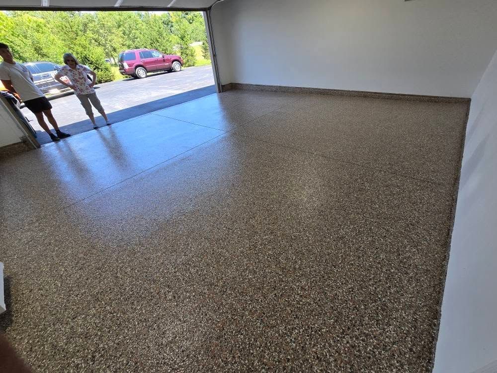 Garage with a speckled floor; two people stand near the open door, a red vehicle is visible outside.
