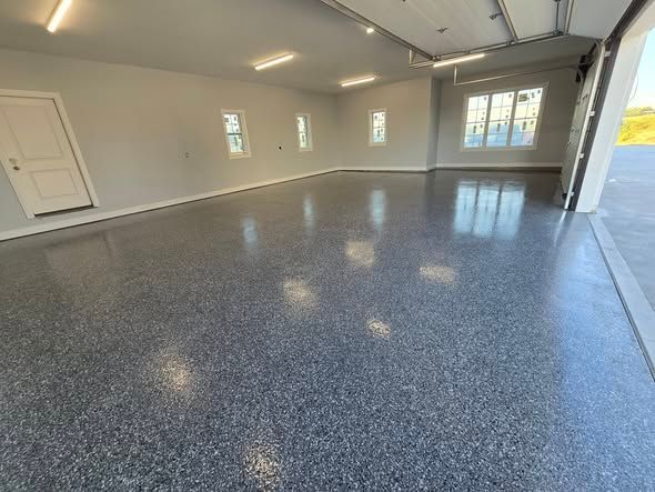 Empty garage with gray speckled epoxy floor and white walls, lit by overhead lights.