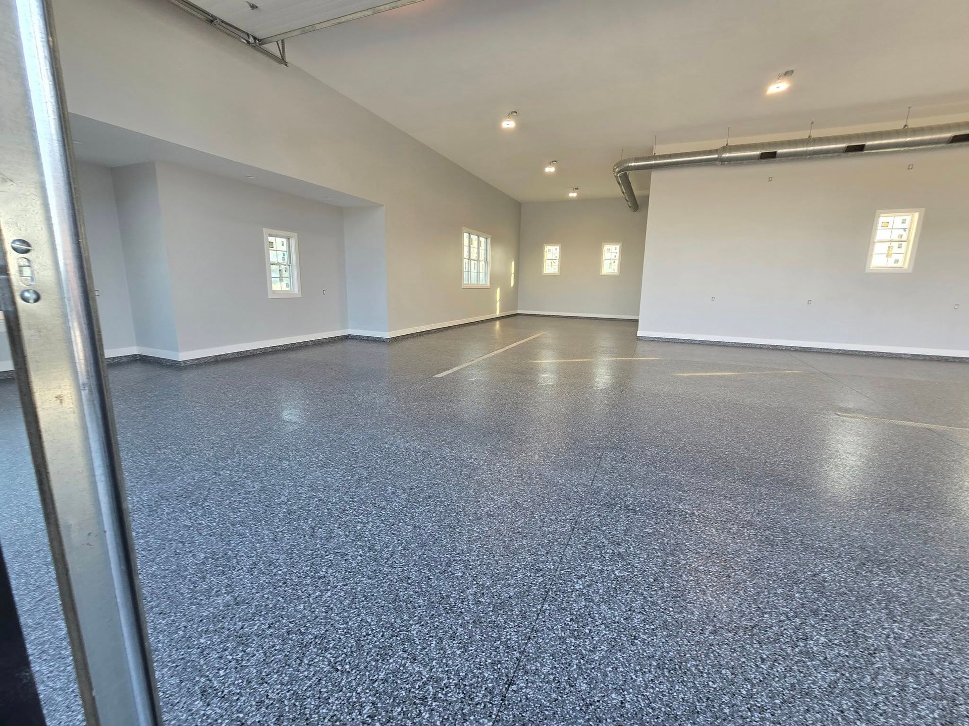 Empty garage with a gray speckled epoxy floor, white walls, and a closed garage door.