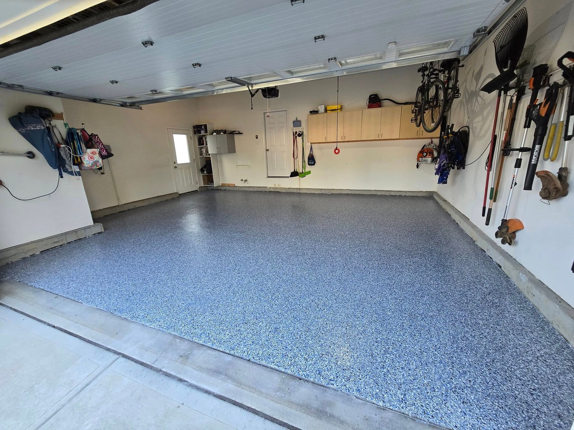 A clean garage with a speckled blue floor. Walls are white, with various storage and equipment.