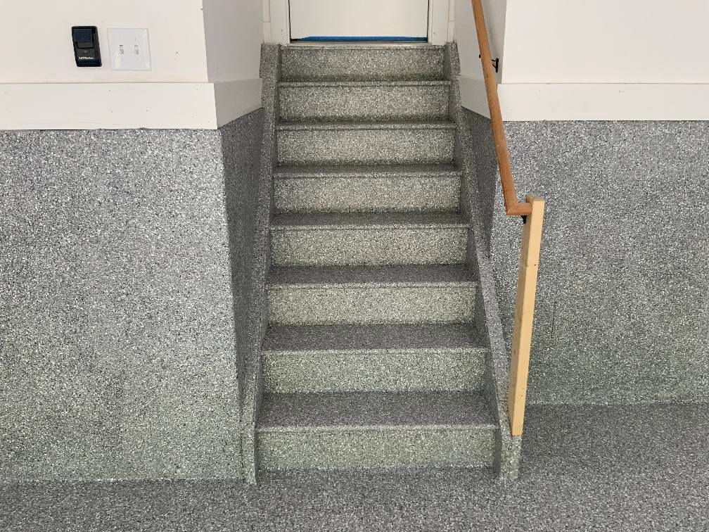 Gray speckled stairs leading up to a doorway, with a wooden handrail and matching walls.