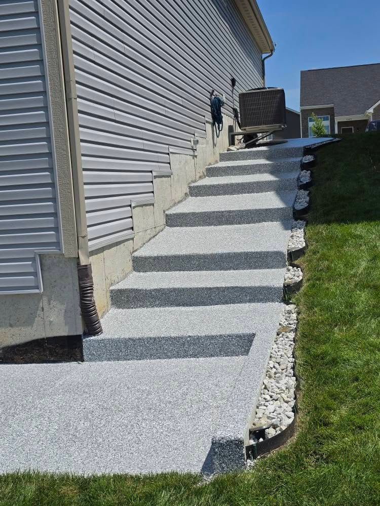 Gray concrete stairs leading up the side of a house with a grassy yard.