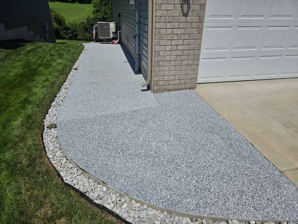 Concrete walkway with stone border next to green lawn and garage.