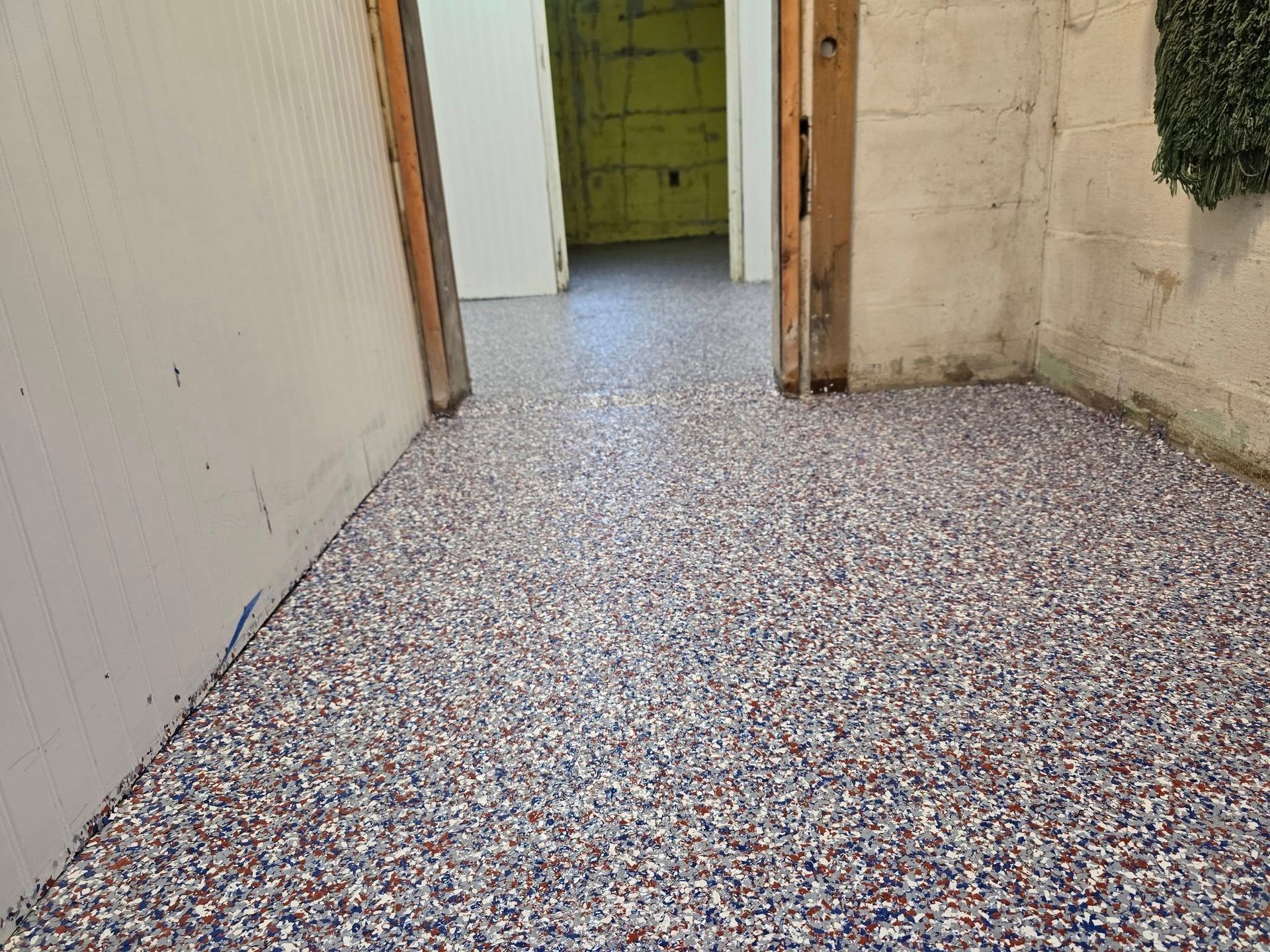 Room with speckled floor, doorway. Walls are white and concrete.