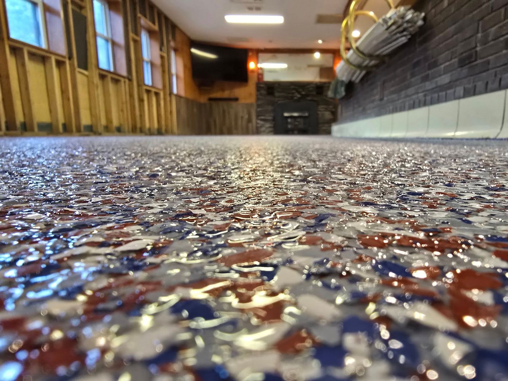 Epoxy floor with red, white, and blue chips in a basement. Fireplace and exposed wall studs visible.