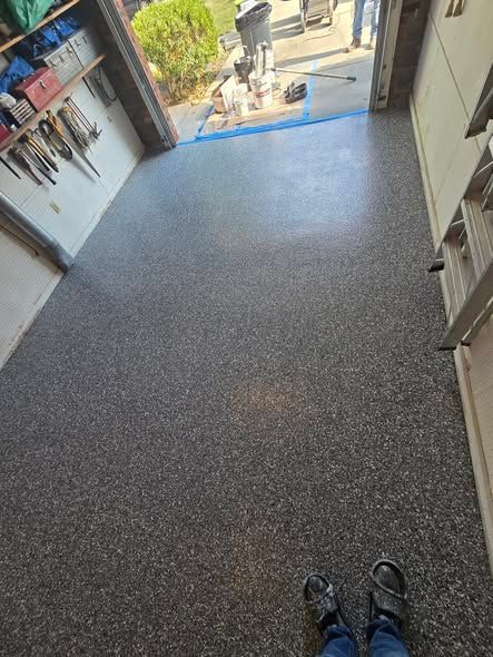 Garage with speckled dark gray epoxy flooring; tools on wall, person's feet visible.