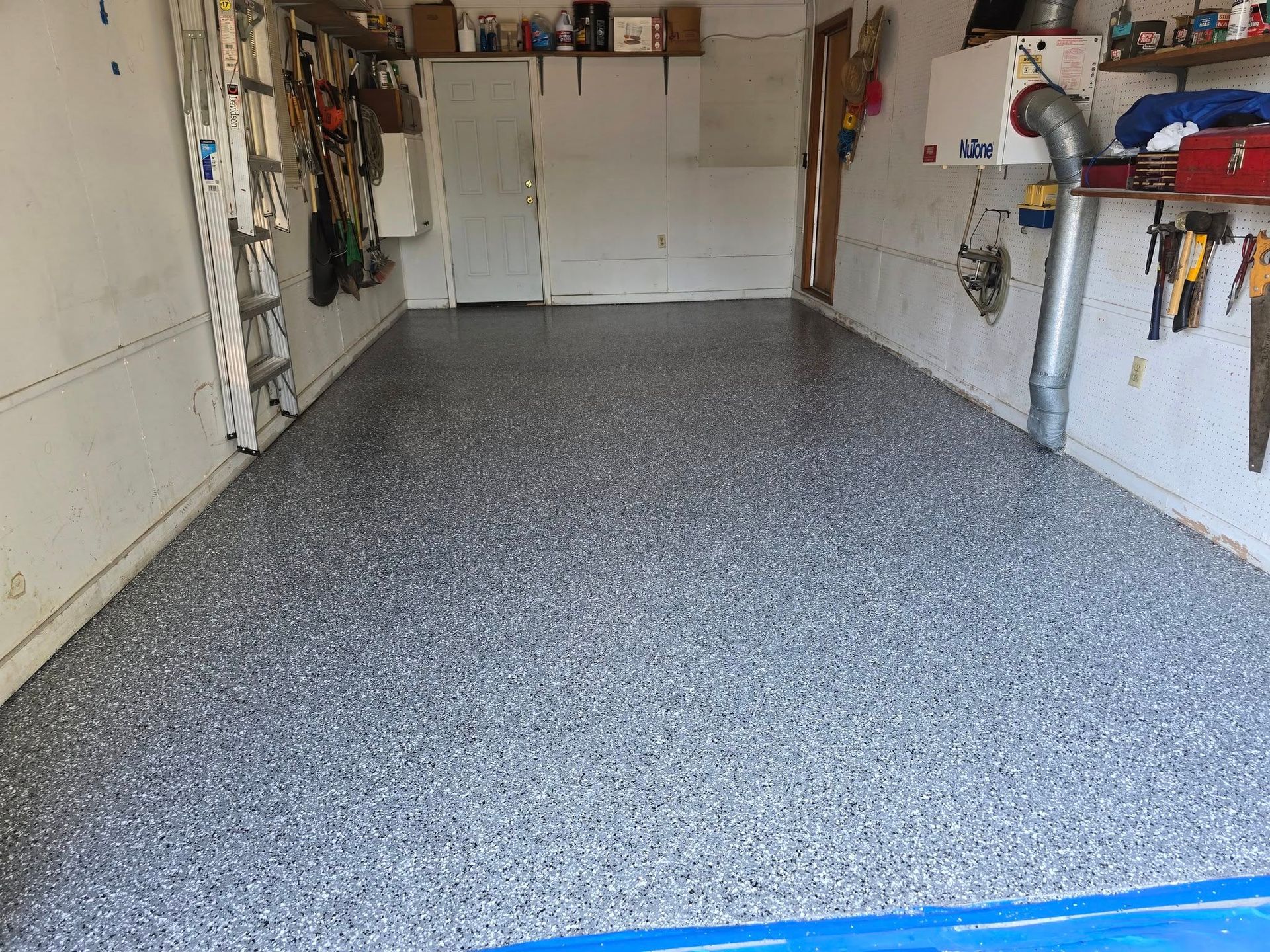 Garage interior with speckled gray epoxy floor, tools on walls, and a closed door.