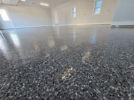 A gray, glossy epoxy garage floor with flecks. The room has white walls and windows.