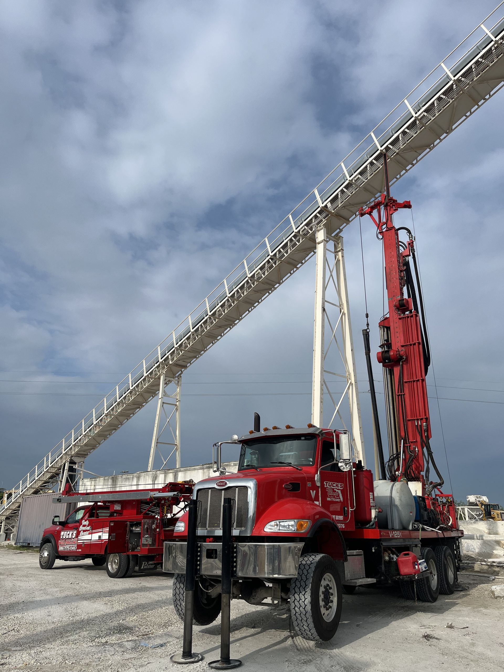 Red fire truck with extended ladder and vertical mast at an outdoor construction site under cloudy sky