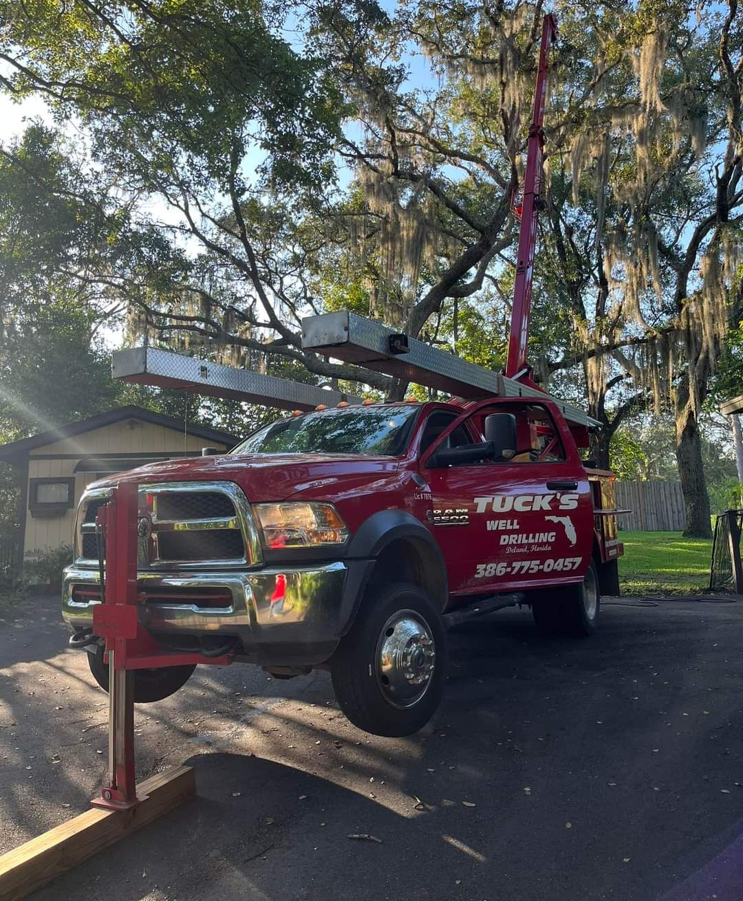 Red tow truck with boom extended on a tree-lined street, lifting a vehicle