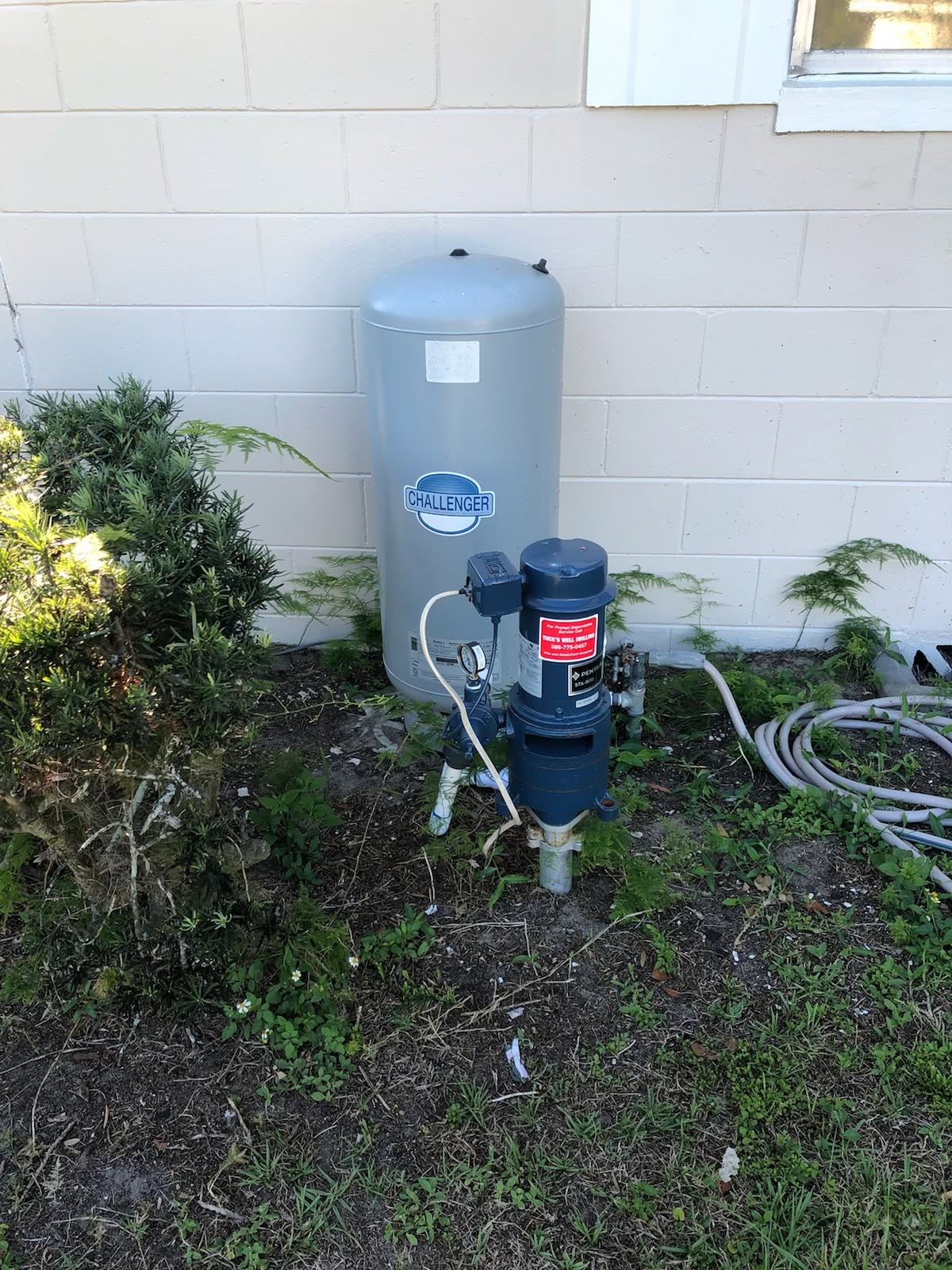 Pool pump and filtration tank beside a house wall, with hoses and grass around them