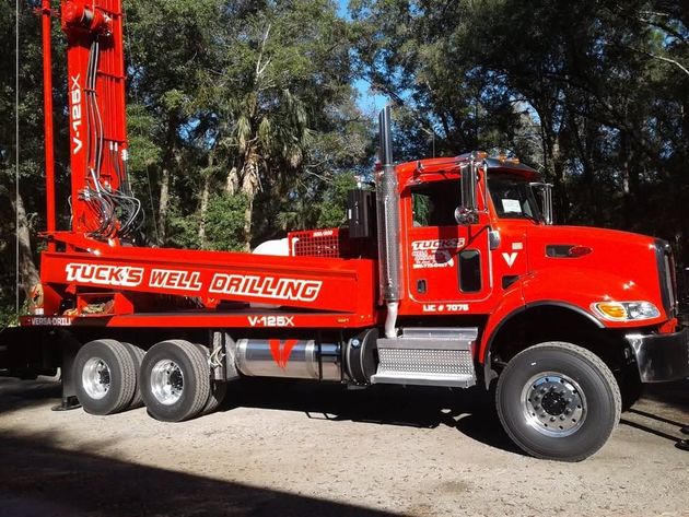 Red drilling truck parked outdoors with trees in the background