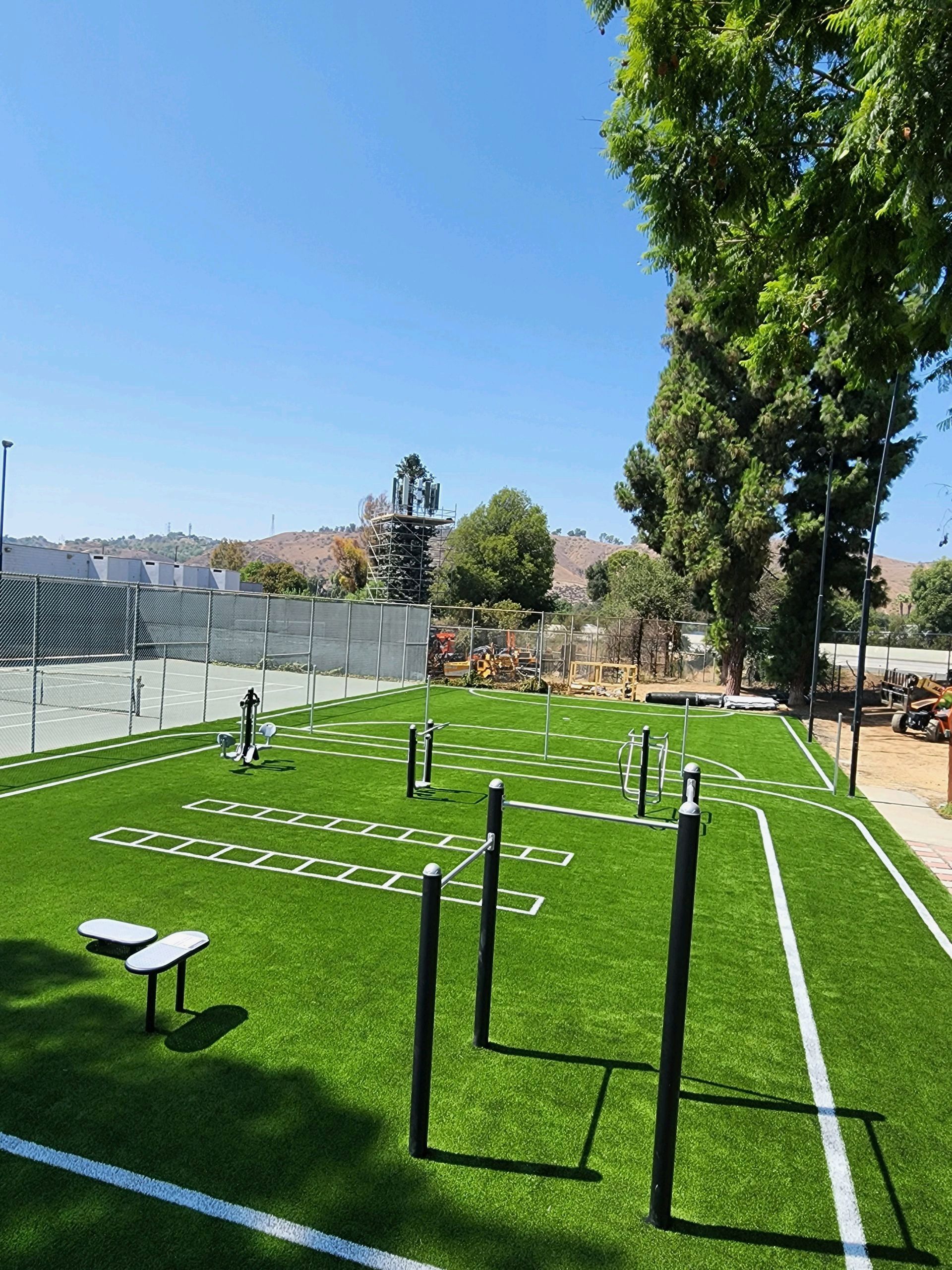 Outdoor fitness area with artificial turf, exercise equipment, and blue sky.