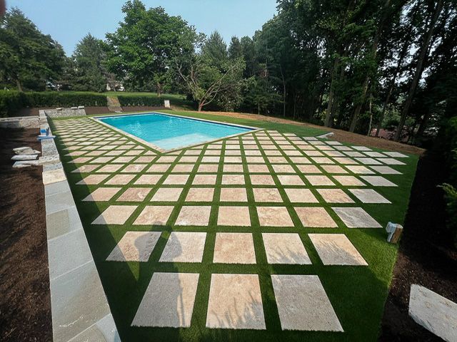 Poolside patio with square stone pavers set in green grass; pool in background.