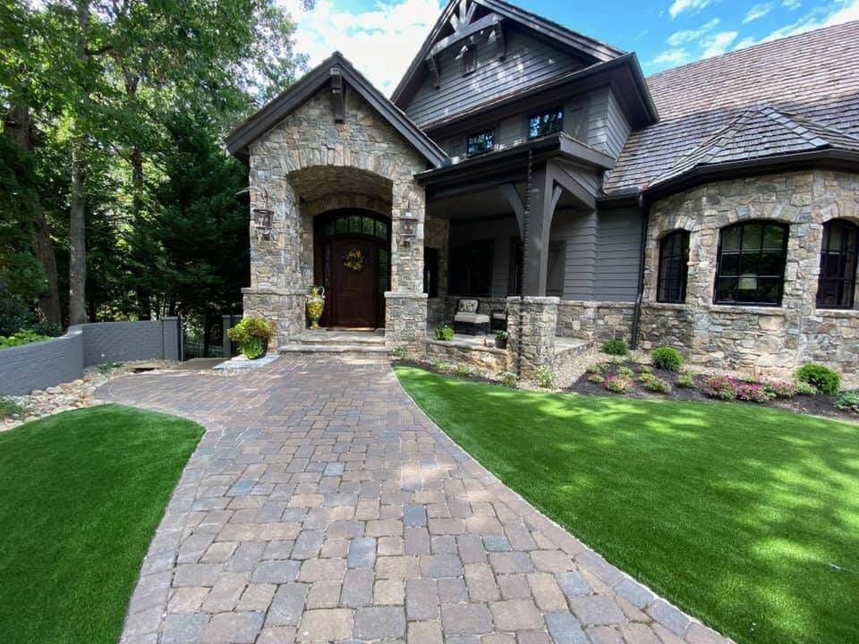 Stone-faced home with a brick pathway and manicured lawn under a sunny sky.