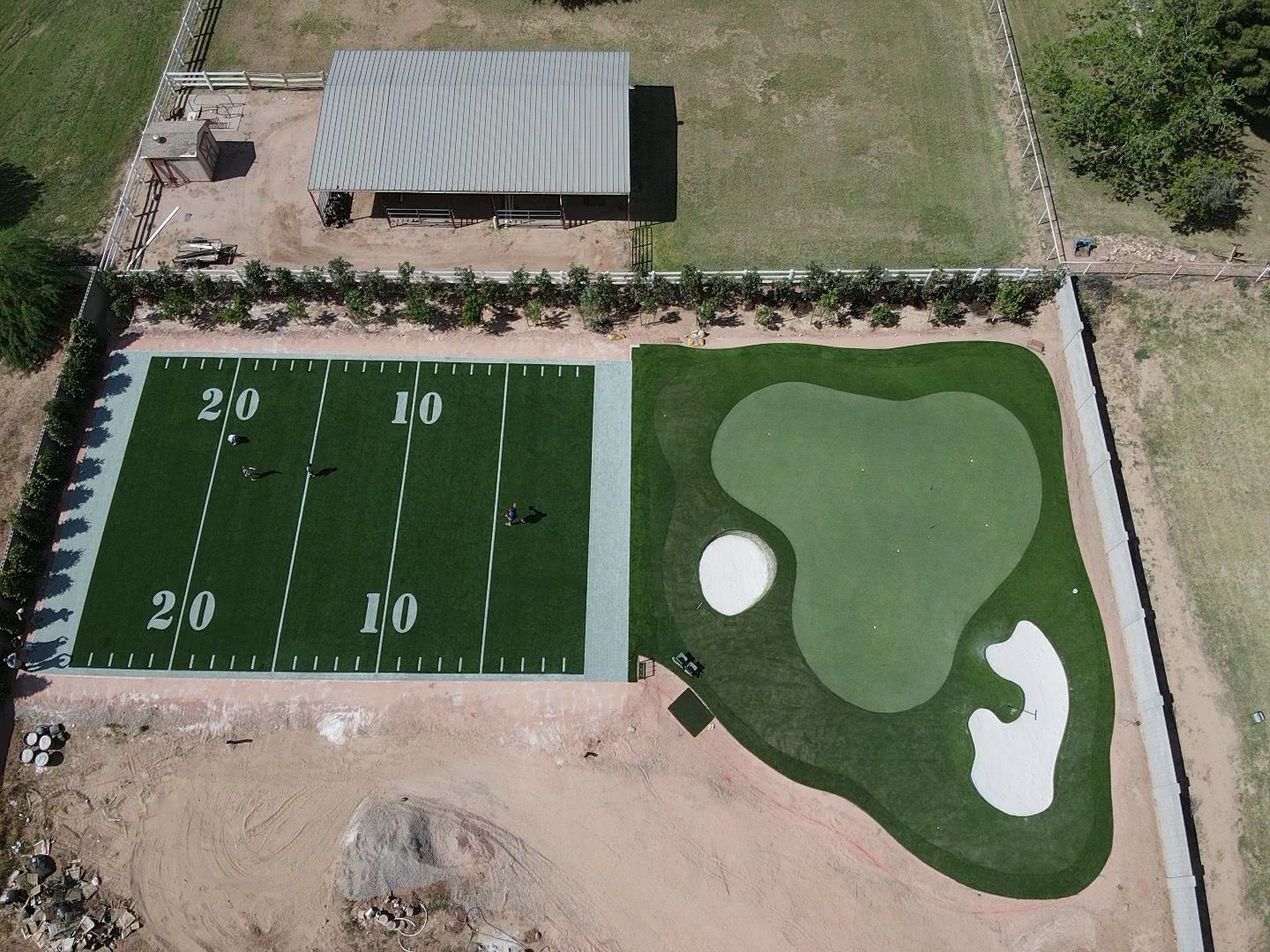 Aerial view: Artificial turf football field and putting green next to a building.