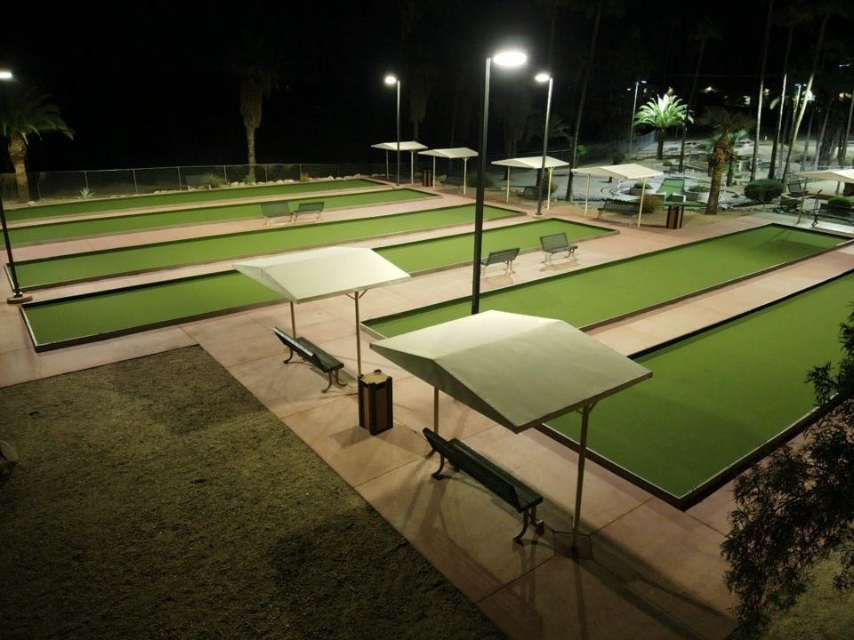 Nighttime view of well-lit bocce ball courts with shade canopies and benches.