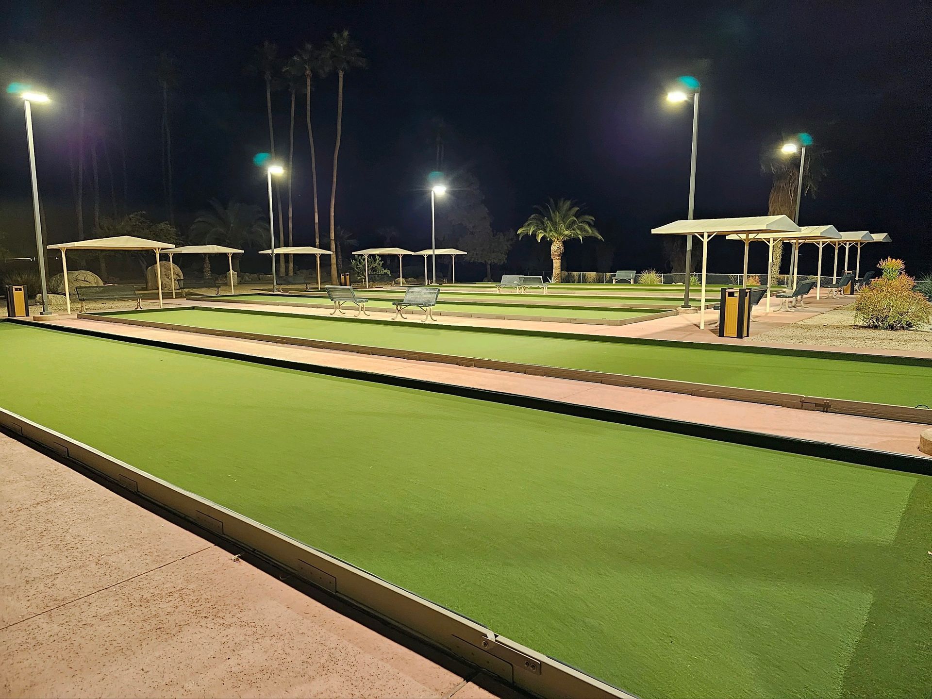 Nighttime bocce ball court with artificial turf, overhead lights, and covered seating.