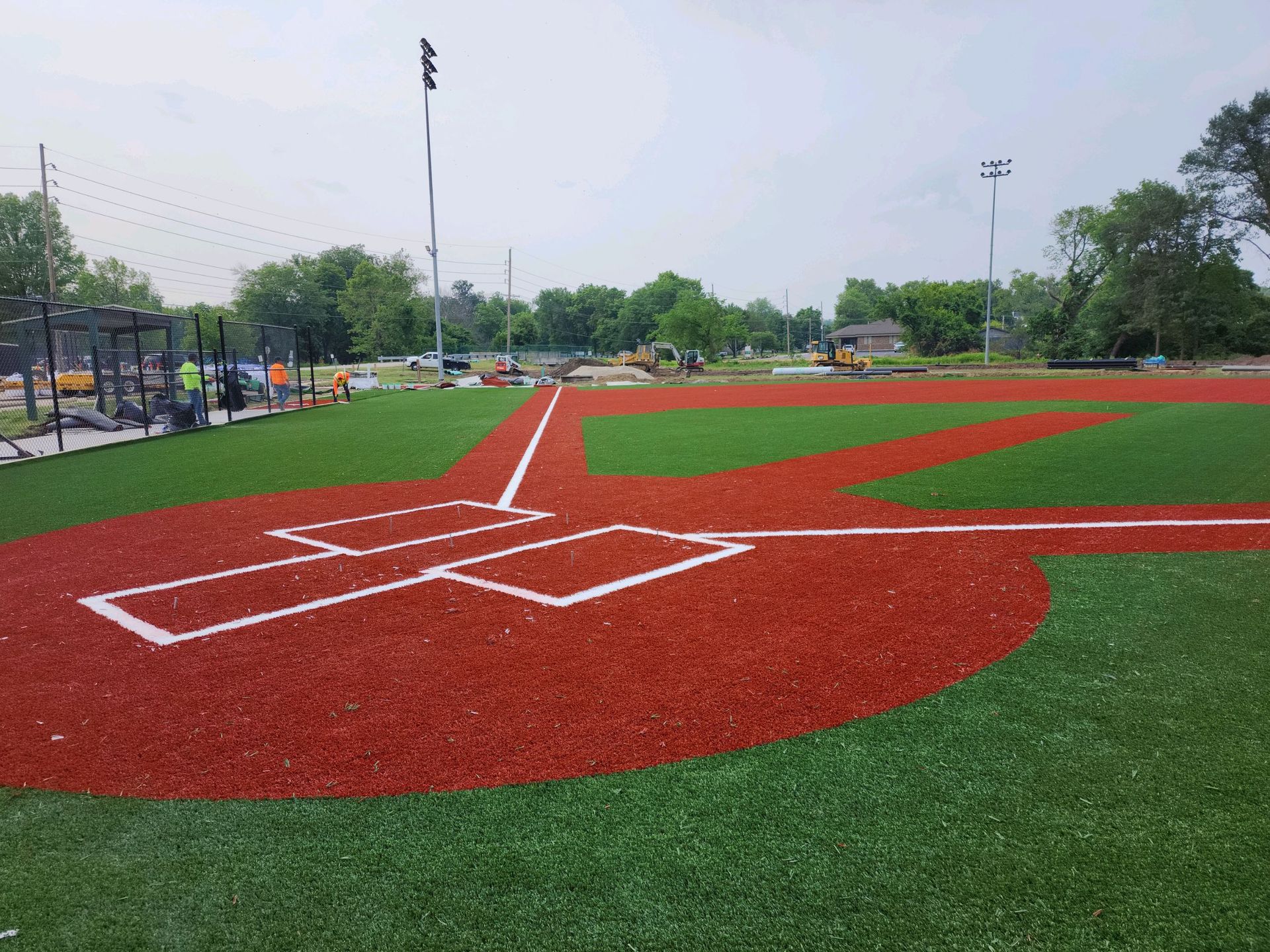 Baseball field with red infield, green outfield, and white base lines. Construction in the background.