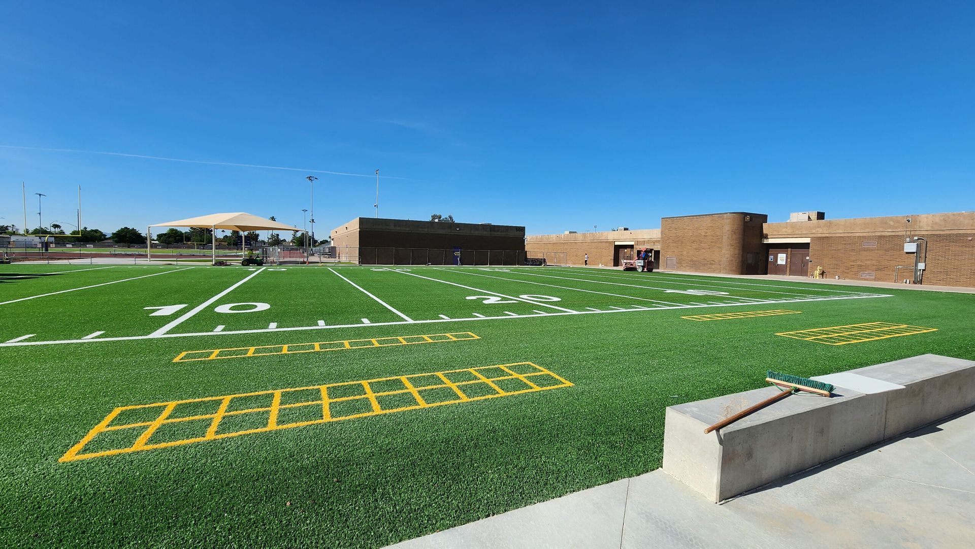 Artificial turf football field with yard lines, end zones, and school building under a blue sky.