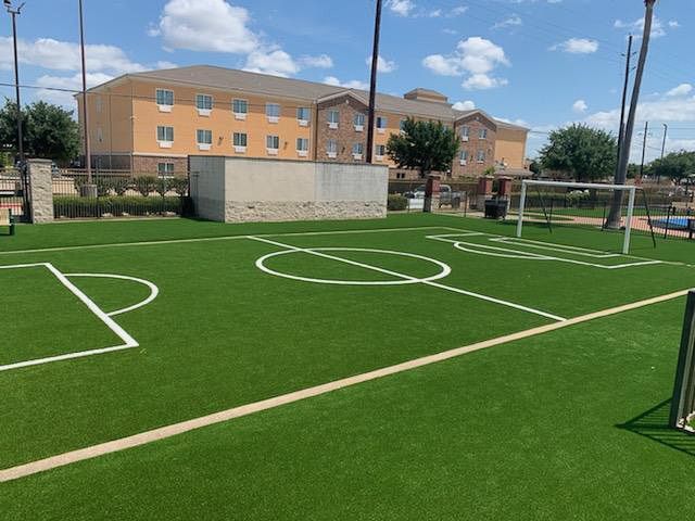 Artificial turf soccer field in front of a tan hotel on a sunny day.