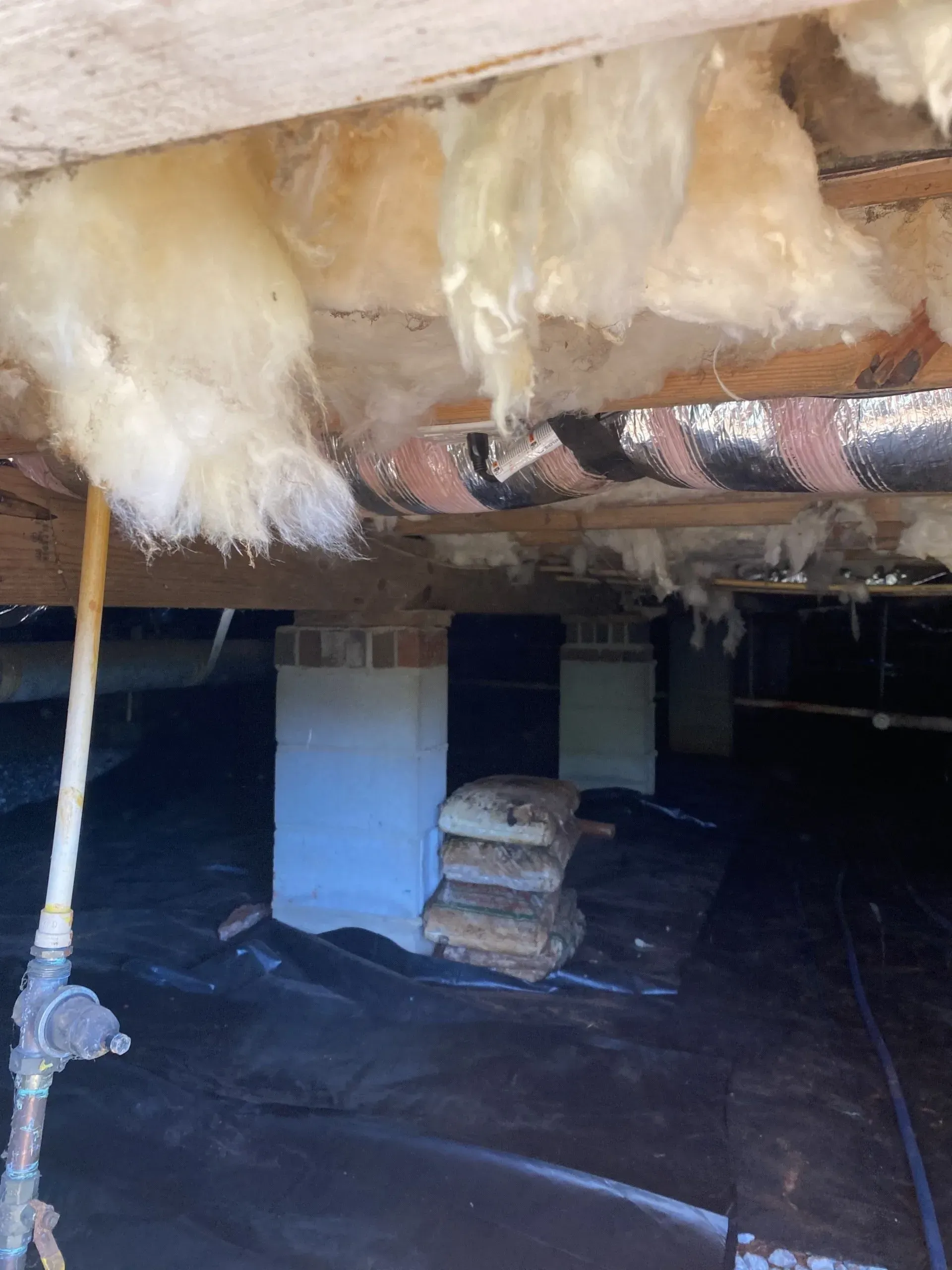 Underneath house with insulation, support pillars, and black tarp ground cover.